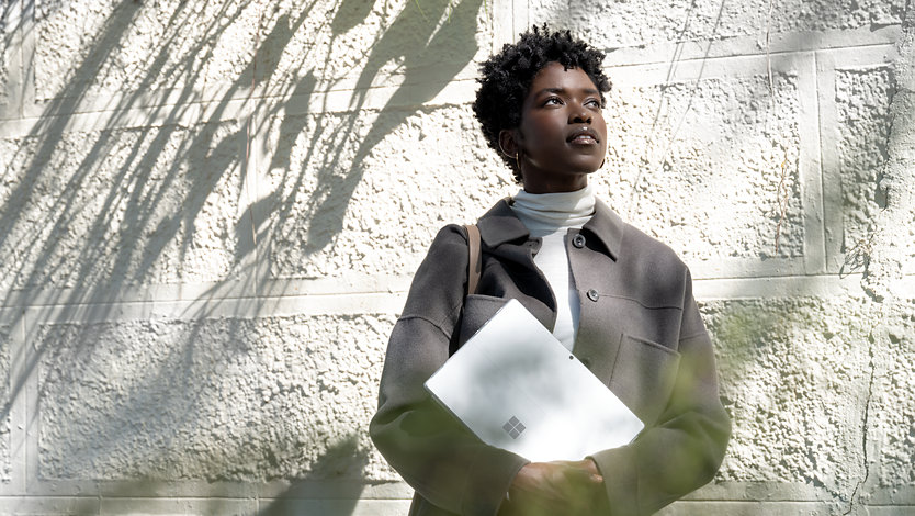 A person standing in front of a wall holding Surface Pro 8.