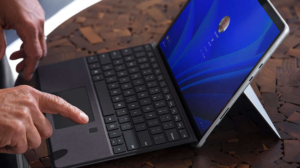 A person's hands interacting with a Surface Pro 8 for Business on a table.