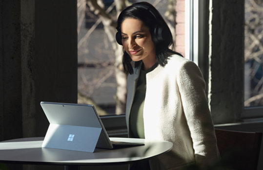 A person with headphones sitting a table with a Surface Pro 8 for business.