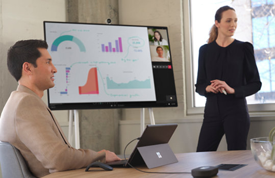 Two people in a conference room using Surface Pro 8 for Business and Surface Hub 2S.