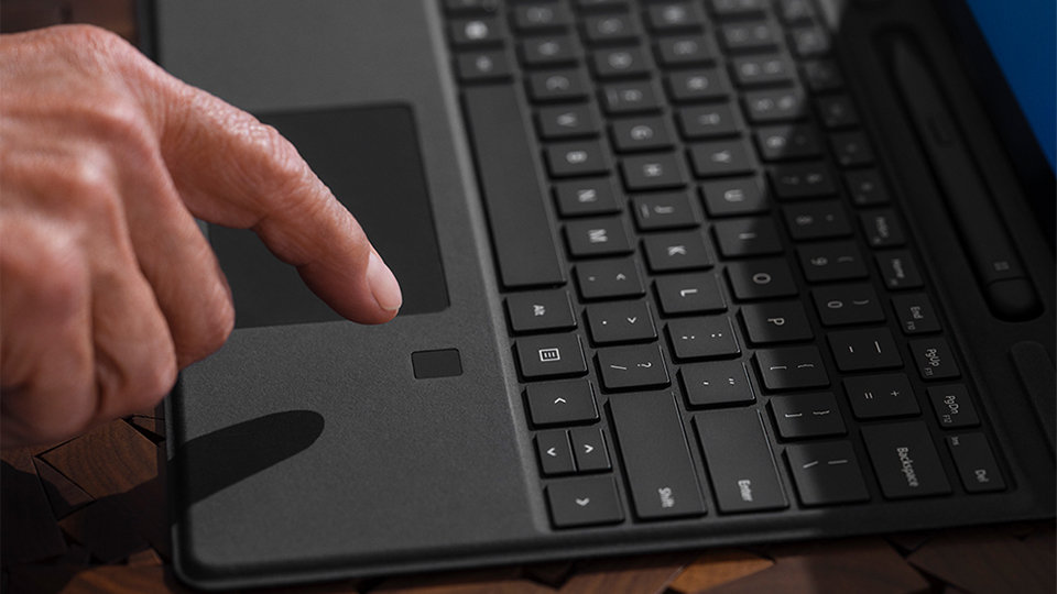 A person's finger just above the fingerprint reader of the Surface Pro Signature Keyboard.