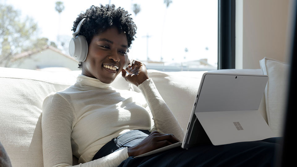 A person seated on a sofa working with a Surface Pro device and Surface Pro Signature Keyboard on their lap.