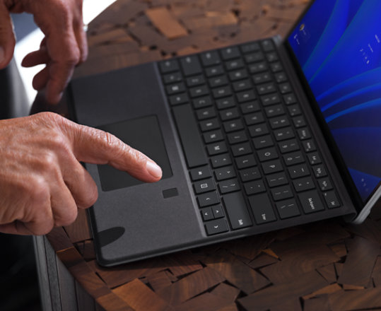 Eine Person meldet sich mit ihrem Fingerabdruck auf dem Surface Pro Signature Keyboard mit Fingerabdruckleser bei einem Surface Laptop an.