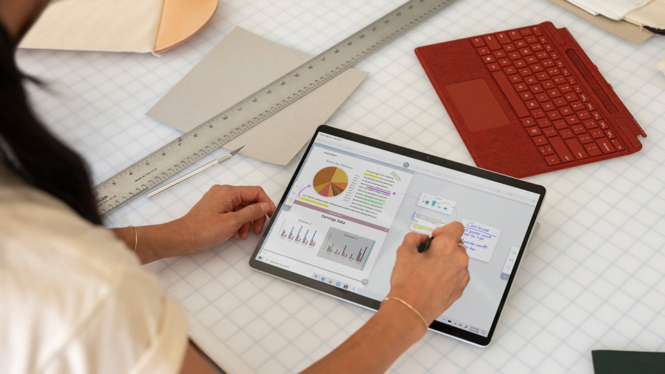 A person using a Surface Pro X with detached Type Cover nearby.