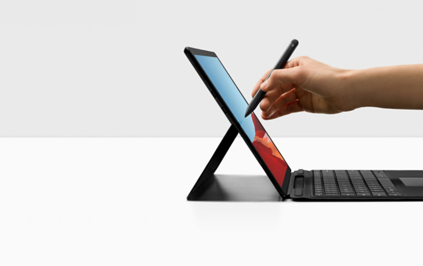 A hand holding Surface Slim Pen writes on the screen of Surface Pro X.