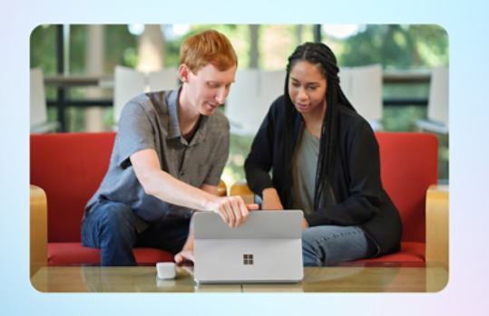 Due studenti osservano lo schermo di un computer Surface platino. Un mouse Surface Arc Mouse grigio chiaro posato sul tavolo. 