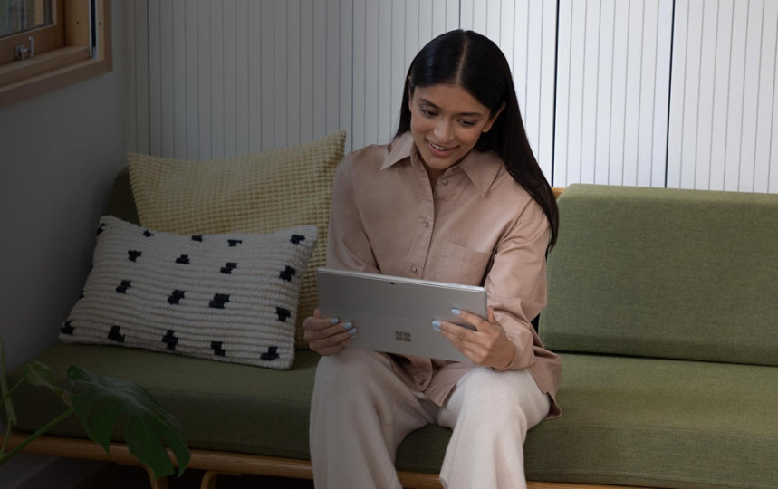 Žena sedící doma na gauči a spokojeně používá Surface Pro 9