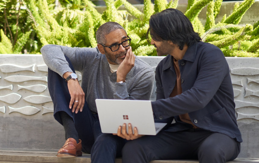 Two people conversing with a laptop outdoors.