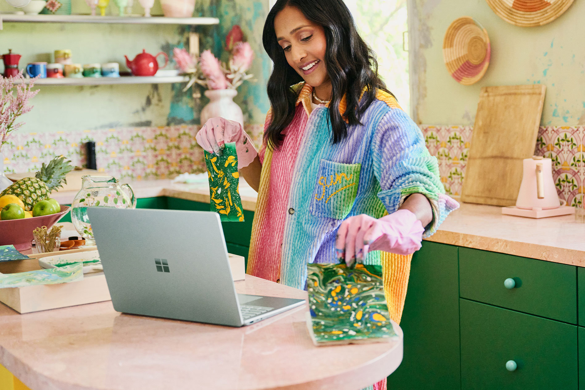 A woman stands at a countertop holding crafts she made in front of the camera of her Surface Laptop 5.