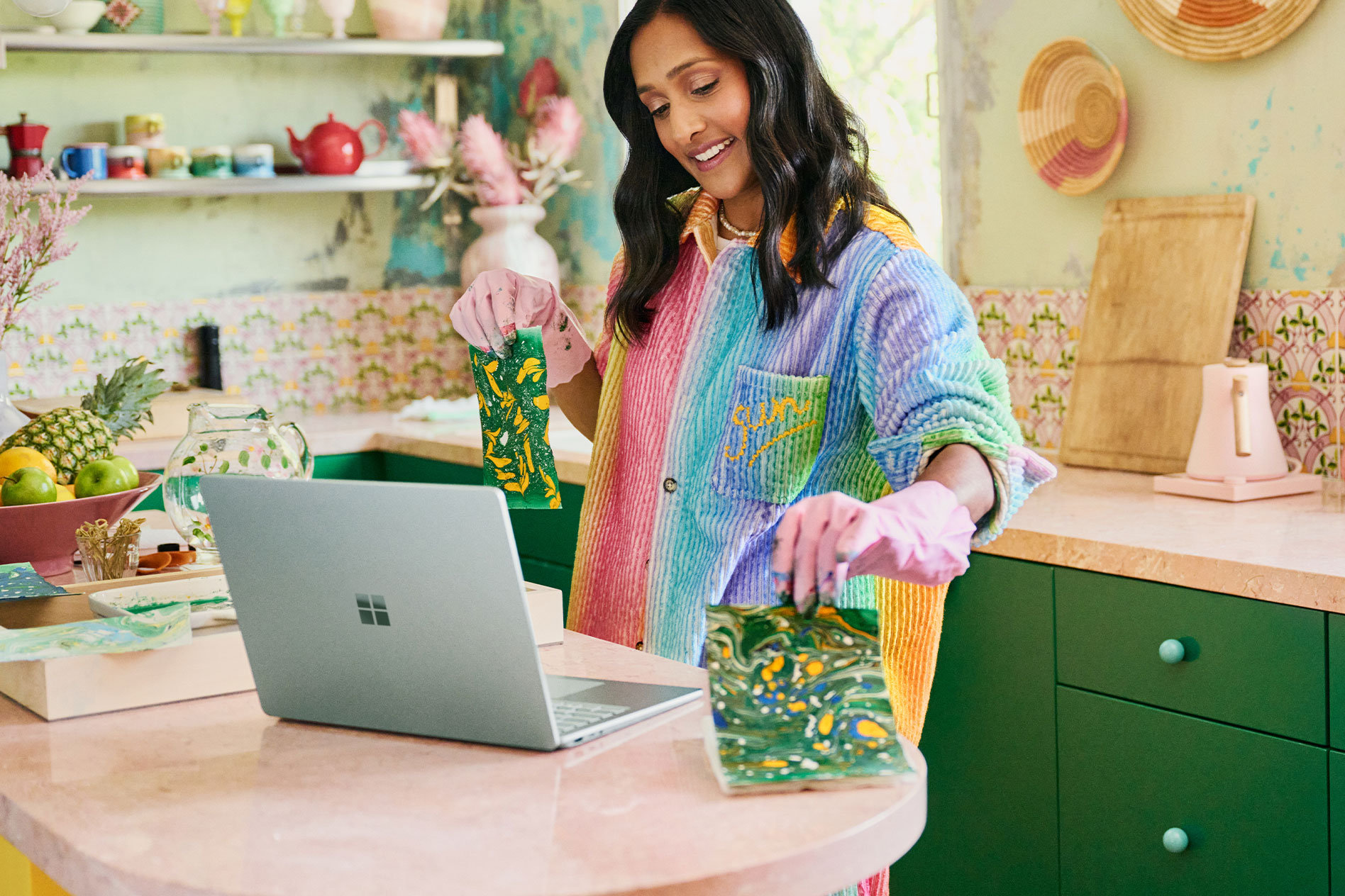 Une femme est debout sur un comptoir et tient des objets artisanaux qu’elle a fabriqués devant l’appareil photo de son Surface Laptop 5.