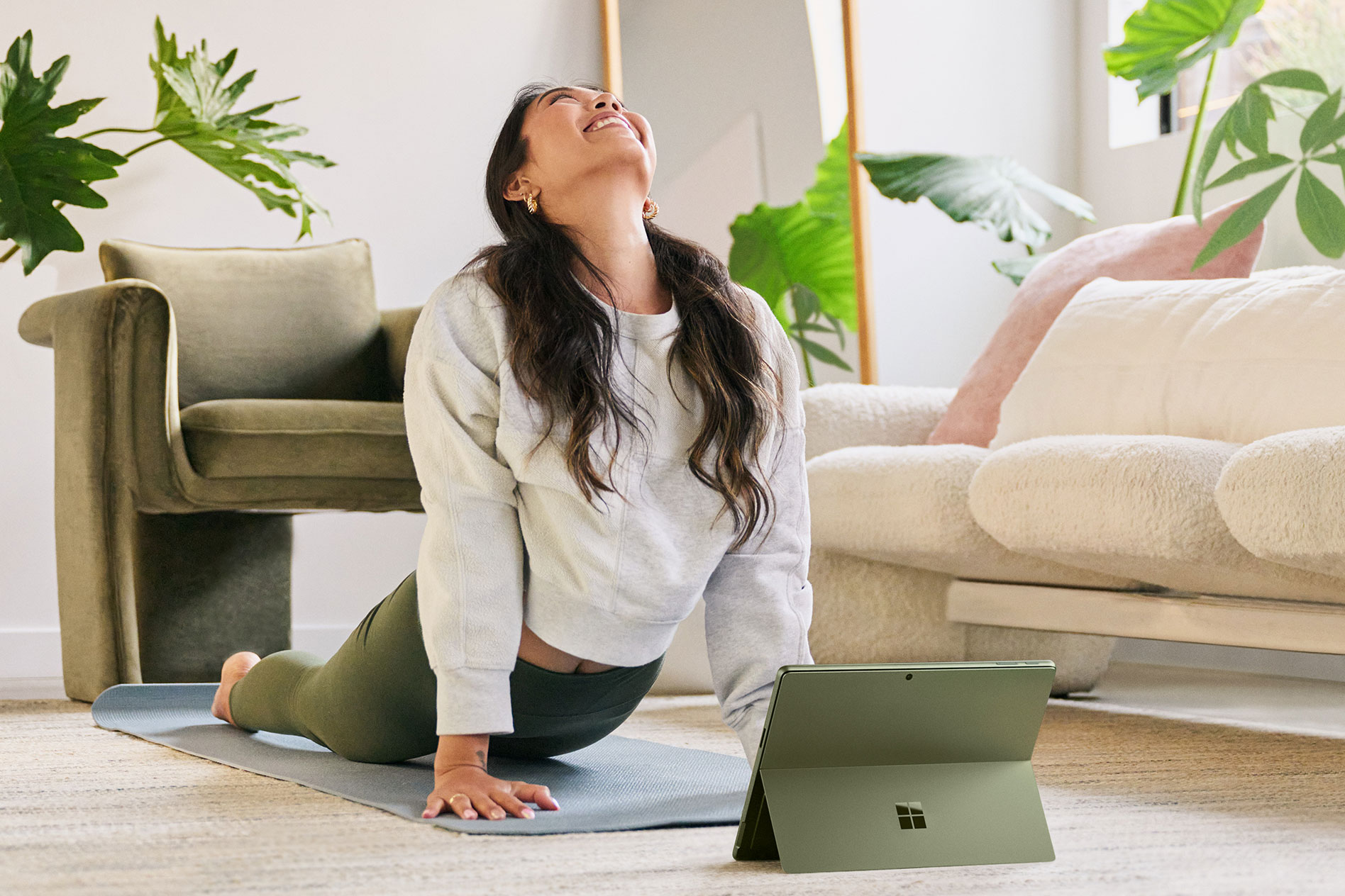 Une femme prend une pose de yoga sur le sol de son salon avec sa Surface Pro 9 juste devant elle.