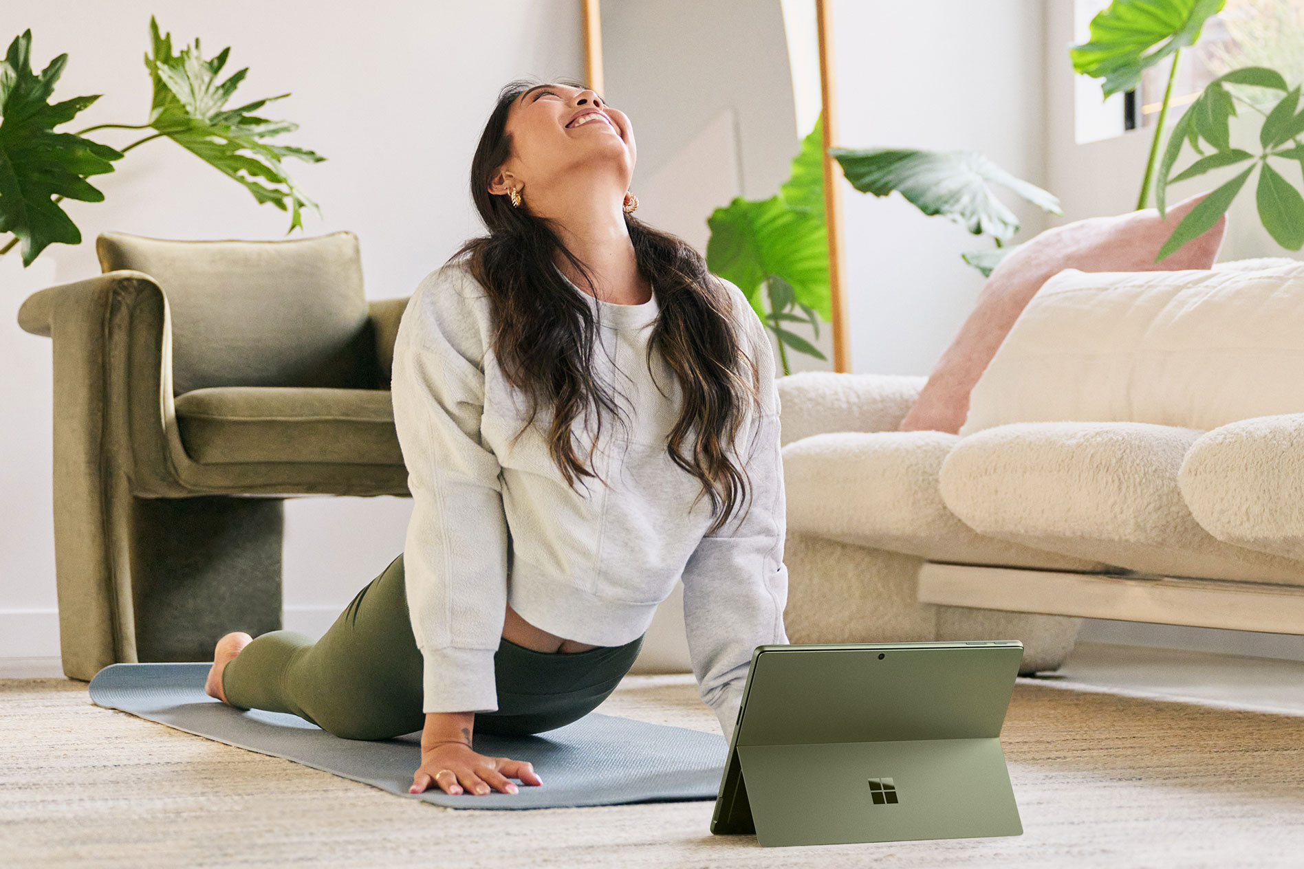 Surface Pro 9 をすぐ目の前に置いて、リビング ルームの床でヨガのポーズをする女性。