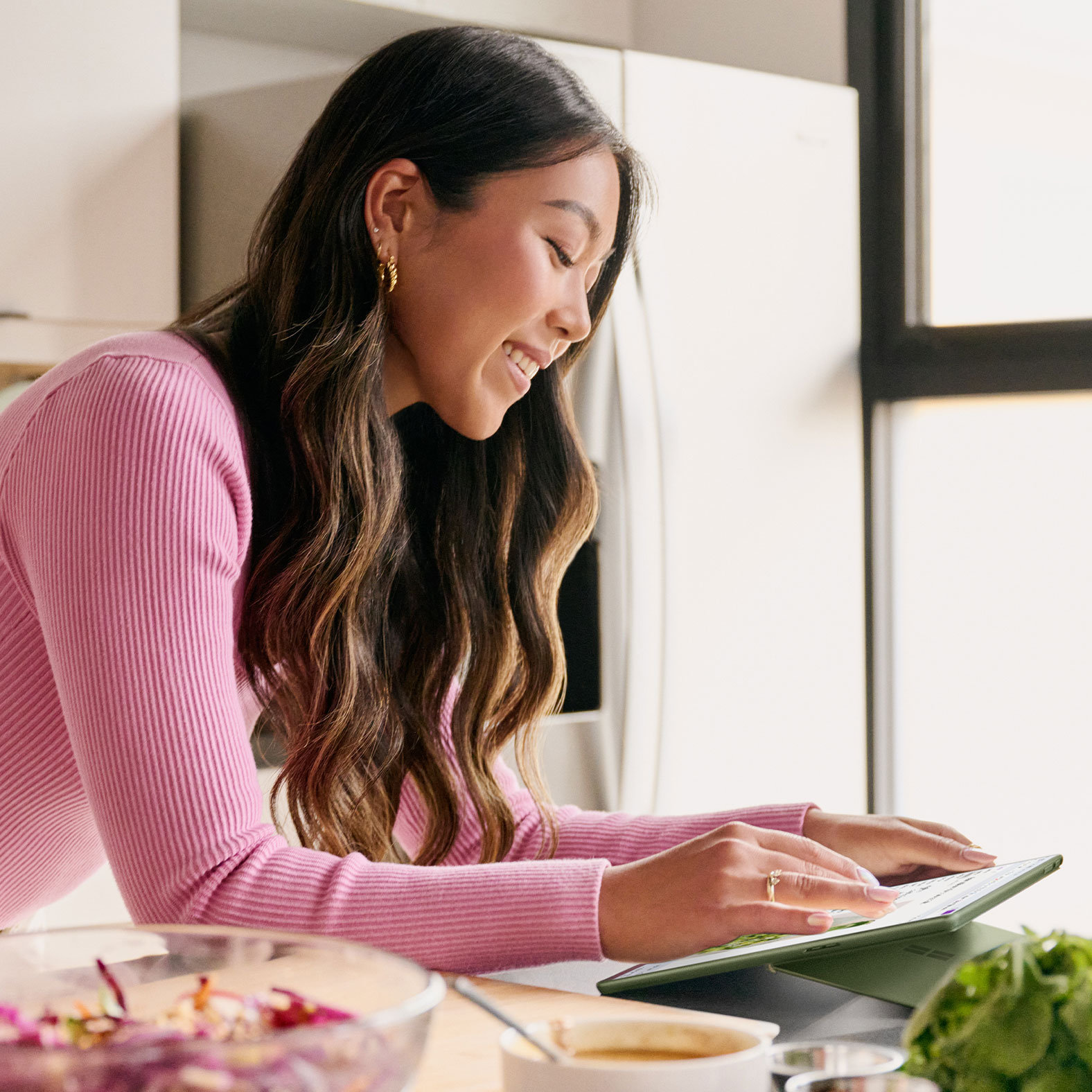 A woman interacts with her Surface Pro 9 touchscreen while preparing a salad in the kitchen.