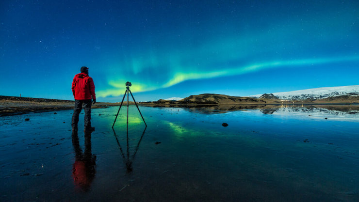A photographer with a tripod camera prepares to capture the Northern Lights.