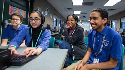 Female volunteer supports students sitting around a computer in a lab.