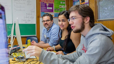 An instructor and a female and male student working in a computer lab.