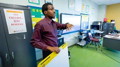 A computer science teacher gives instruction in the front of a classroom.