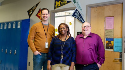 Three teachers smiling at the camera in a school hallway.