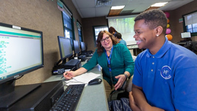 Female teacher supports male student with block coding exercise.