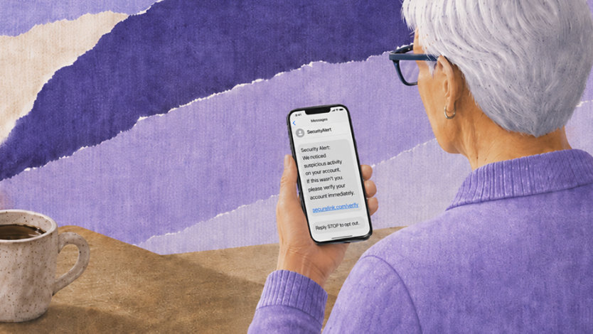 Older woman looking at a smartphone displaying a suspicious security alert text message with a verification link, seated at a table with a coffee mug nearby.