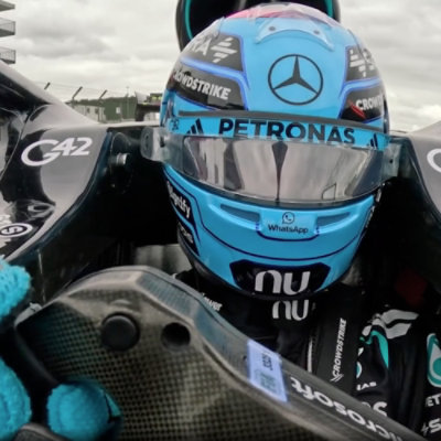 Formula One driver seated in a race car wearing a helmet.
