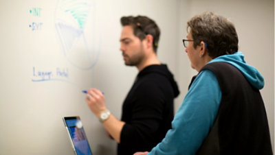 Deux personnes parlant pendant que l’une d’elles écrit sur un tableau blanc.