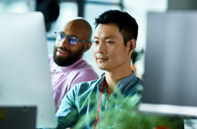 Două persoane stând alături, uitându-se la un monitor desktop.