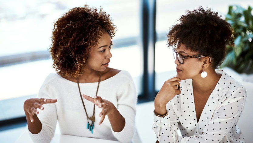 Two colleagues in a modern office discussing work together during a planning conversation.