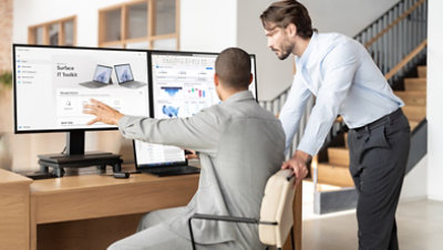 Two colleagues working together at a desk reviewing content on a laptop and desktop monitors.