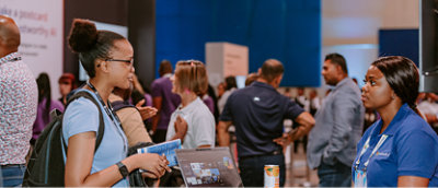 A group of people gathered in a room with various objects visible, including a can of soda on a table and a laptop nearby.