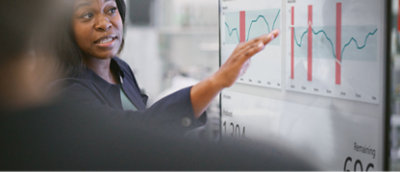 A woman pointing at a graph on a transparent board.