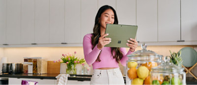 A woman using a tablet in a kitchen with glass jars of fruits nearby.