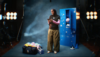 Person in sportswear standing by lockers while using a smartphone in a studio setting.
