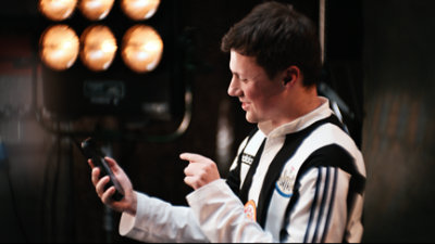 Person wearing a black-and-white striped football jersey pointing at a smartphone