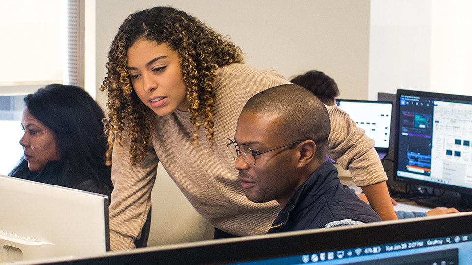 Two coworkers look at a computer monitor together.