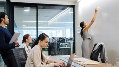 אישה כותבת על לוח ציור בחדר ישיבות עם עמיתים לעבודה