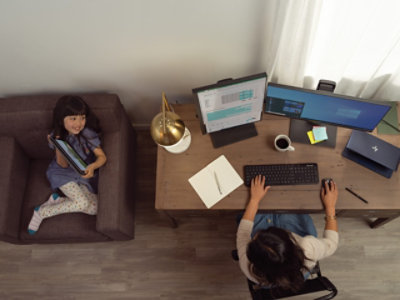 Una persona lavora alla scrivania con due monitor per computer, una tastiera, una tazza di caffè e alcuni articoli da ufficio.