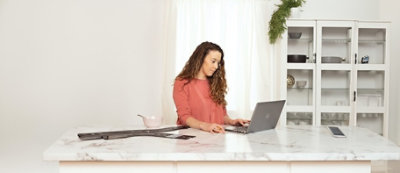 אישה משתמשת במחשב נישא ליד דלפק מטבח כשבקרבת מקום ישנו ילד.