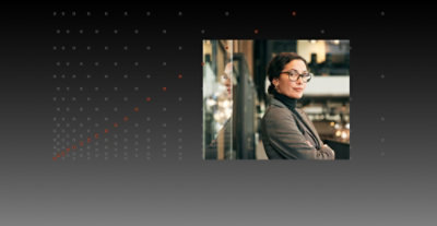 A woman wearing glasses and a suit standing in front of a black and white background with dots.