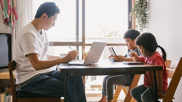 男性が自宅で仕事をしている間、2 人の幼い子供が一緒のテーブルでタブレットを使用しています