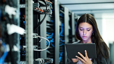 一个人在服务器机房里手持平板电脑的画面。