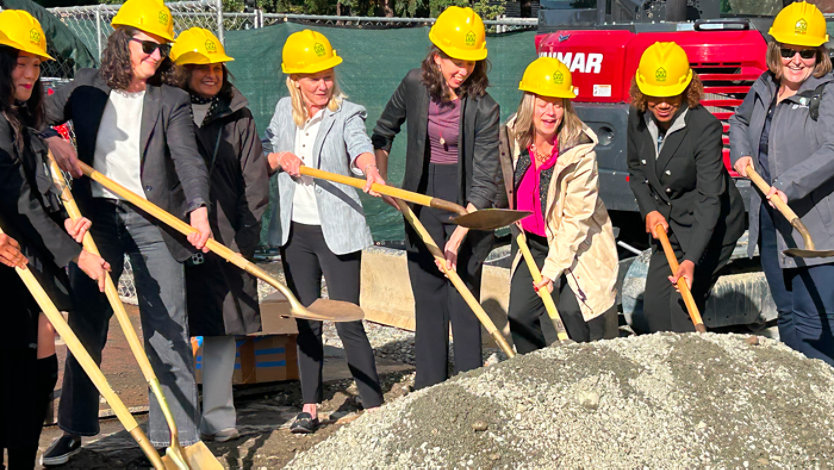 Local elected leaders and business and nonprofit advocates for affordable housing participate in an outdoor ceremonial groundbreaking for Plymouth Housing. They wear hard-hats and are holding shovels painted gold.