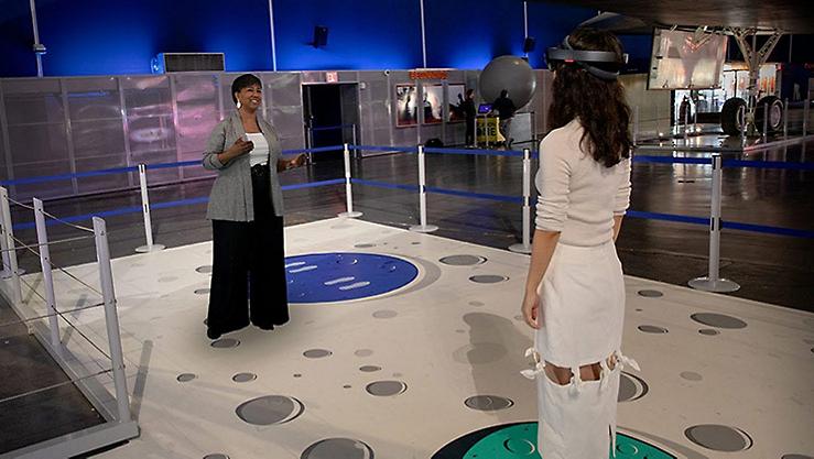 Two women standing in a roped-off area, one wearing a VR headset
