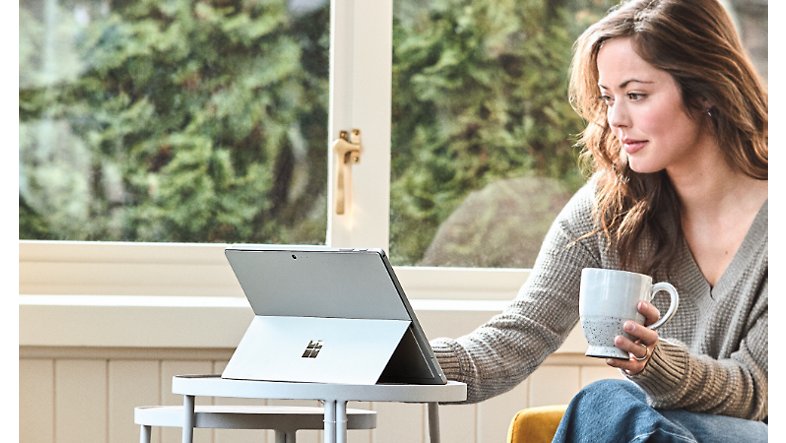 Person holding a coffee cup seated at a small table using a Surface Pro 6