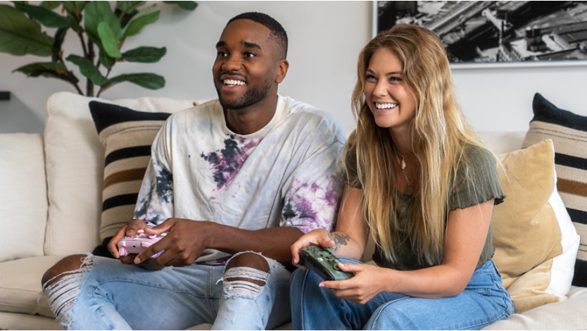 Two friends play Xbox games together while sitting on a couch.