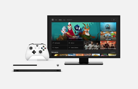 An Xbox console in white next to monitor with Xbox home menu on screen.