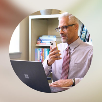 En mann som holder en telefon og ser på en bærbar datamaskin.