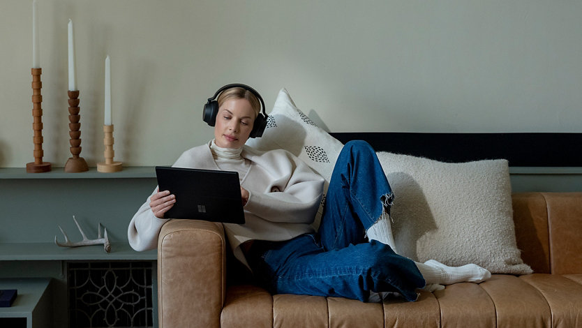 A person relaxing on a couch using Surface Pro 7+ as a tablet.
