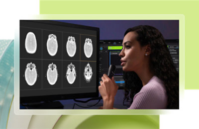 A woman holding a microphone in front of a computer screen displaying x-ray images.