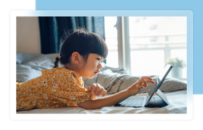 Bambino con una camicia floreale che utilizza un tablet mentre è sdraiato su un letto in una stanza luminosa.